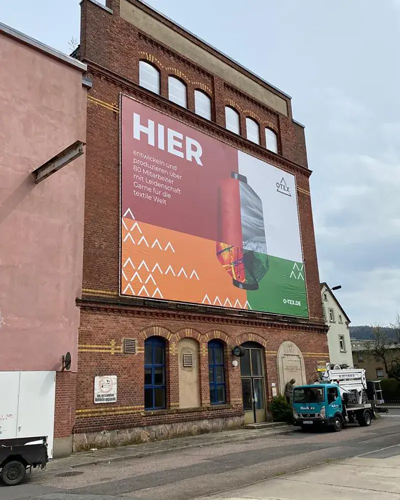 Fertig montiertes 20 × 8 Meter großes OTEX-Riesenposter am Werksgebäude in Flöha