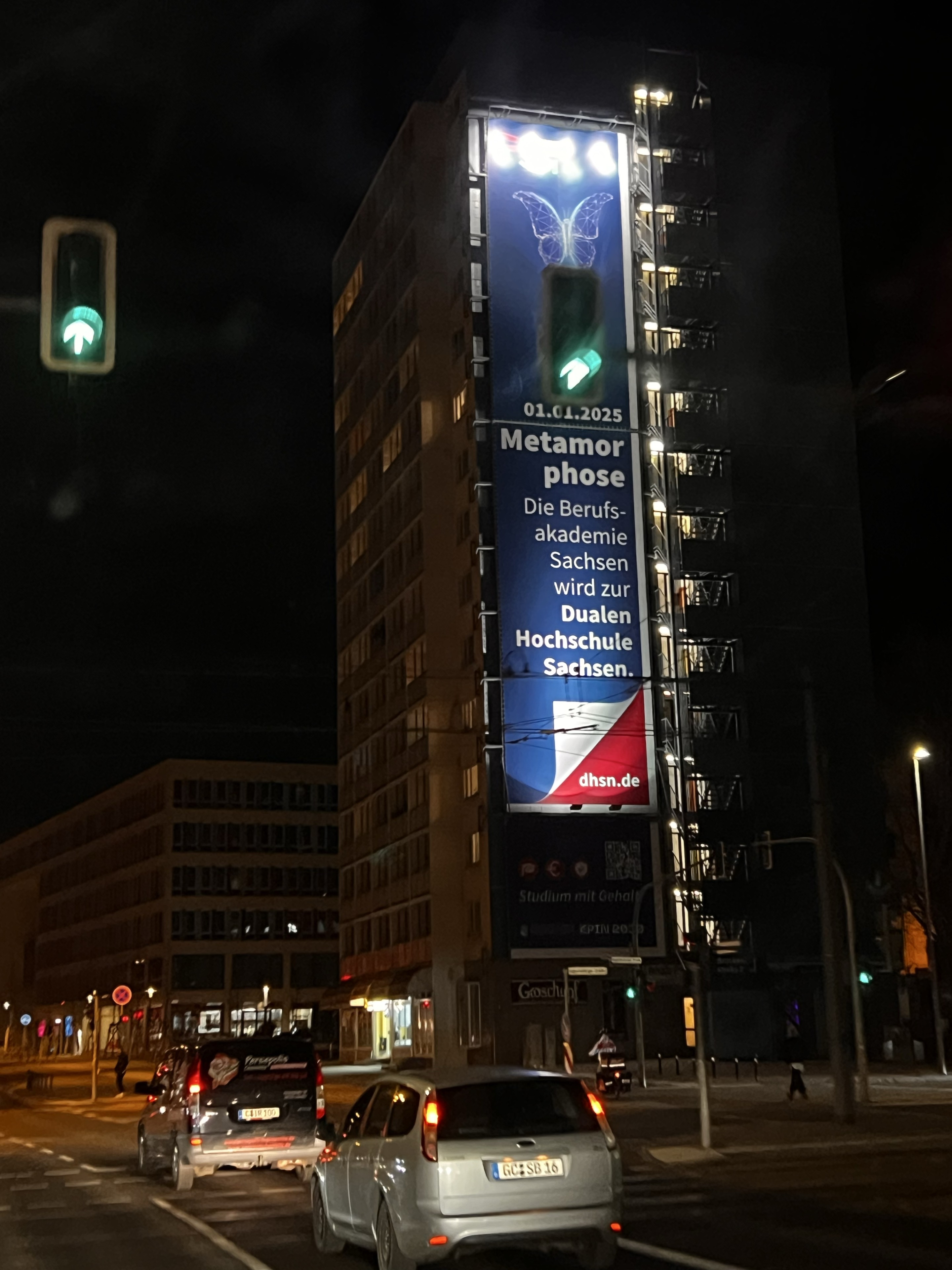 Beleuchtetes blaues Metamorphose-Plakat der Dualen Hochschule Sachsen am MEGA bei Nacht