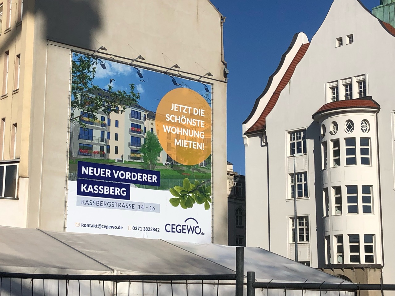 Seitliche Ansicht des CEGEWO-Plakats mit Wohnanlage und orangefarbener Mietbotschaft