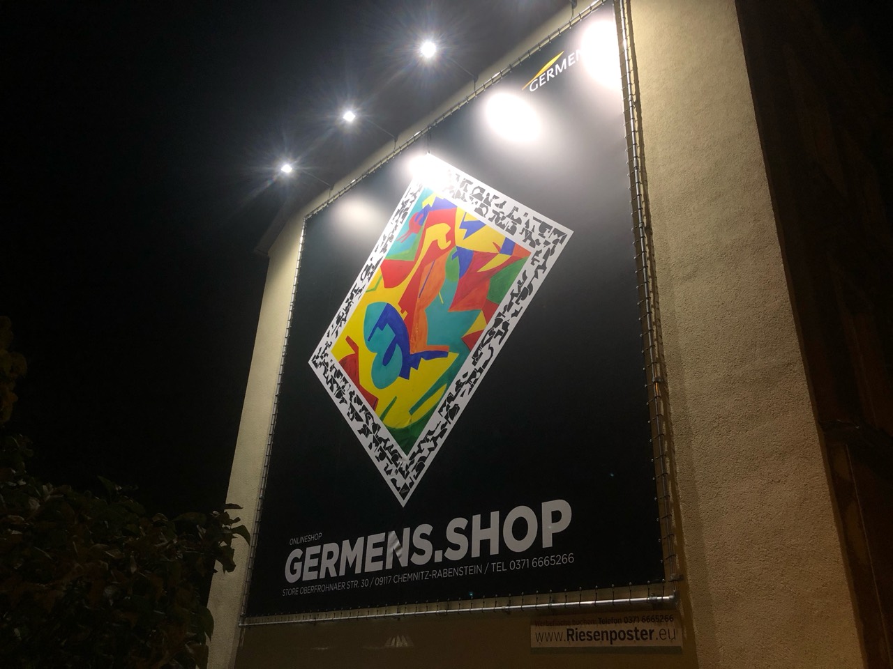 Beleuchtetes GERMENS-Riesenposter mit farbigem Kunstmotiv und großem Schriftzug GERMENS.SHOP