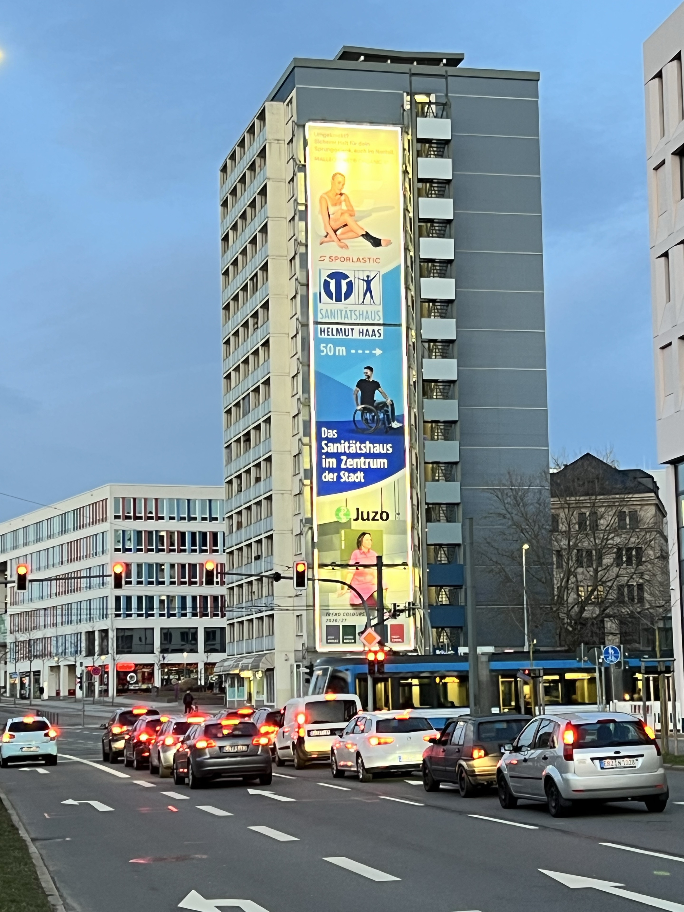 Beleuchtetes Riesenposter von Sanitätshaus Helmut Haas am MEGA Ad Tower in der Dämmerung