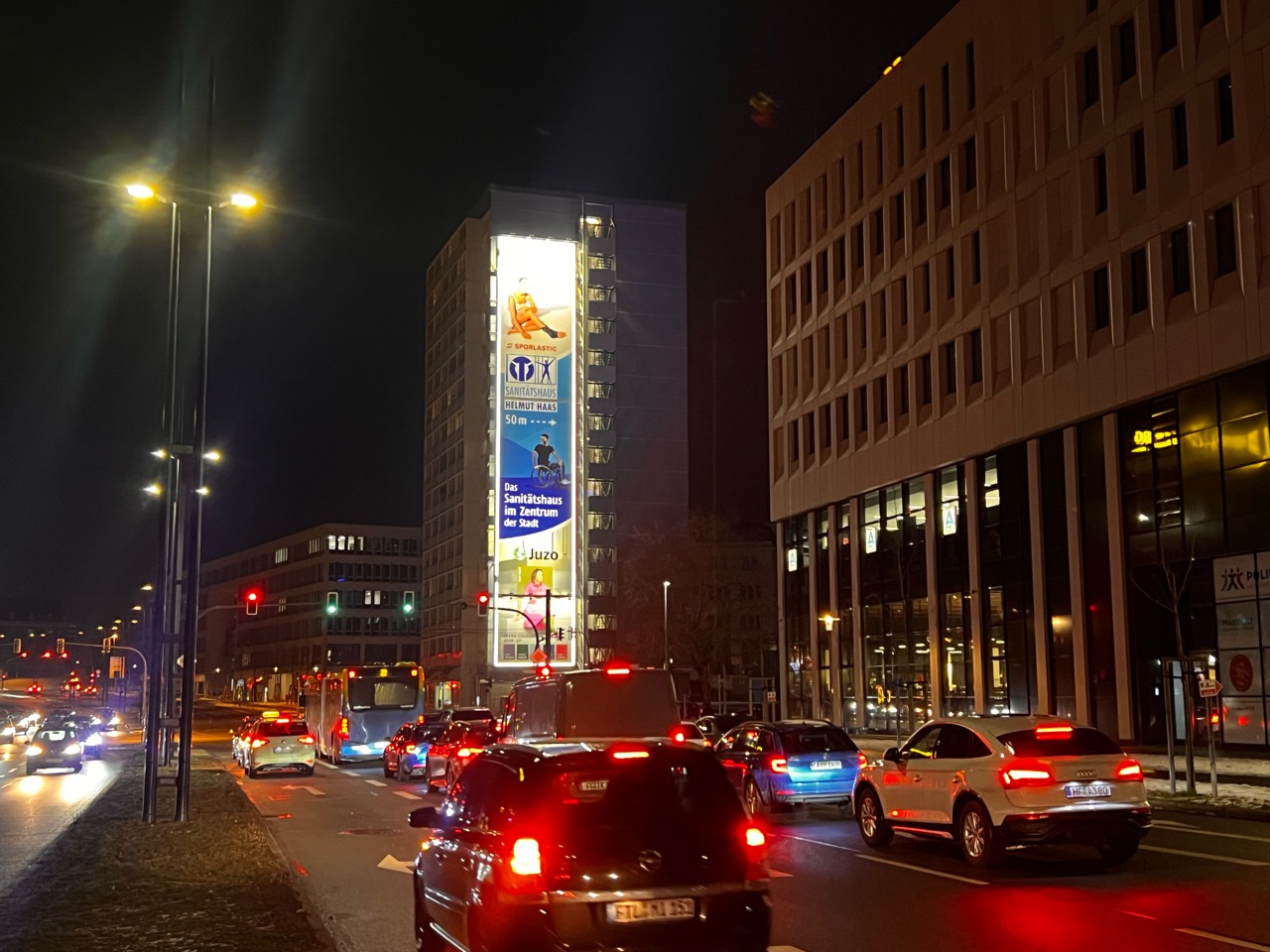 Haas-Riesenposter am beleuchteten MEGA Ad Tower über dem nächtlichen Straßenverkehr