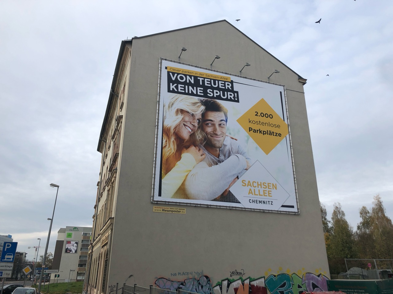 Sachsen-Allee-Plakat mit zwei lächelnden Personen und Hinweis auf kostenlose Parkplätze