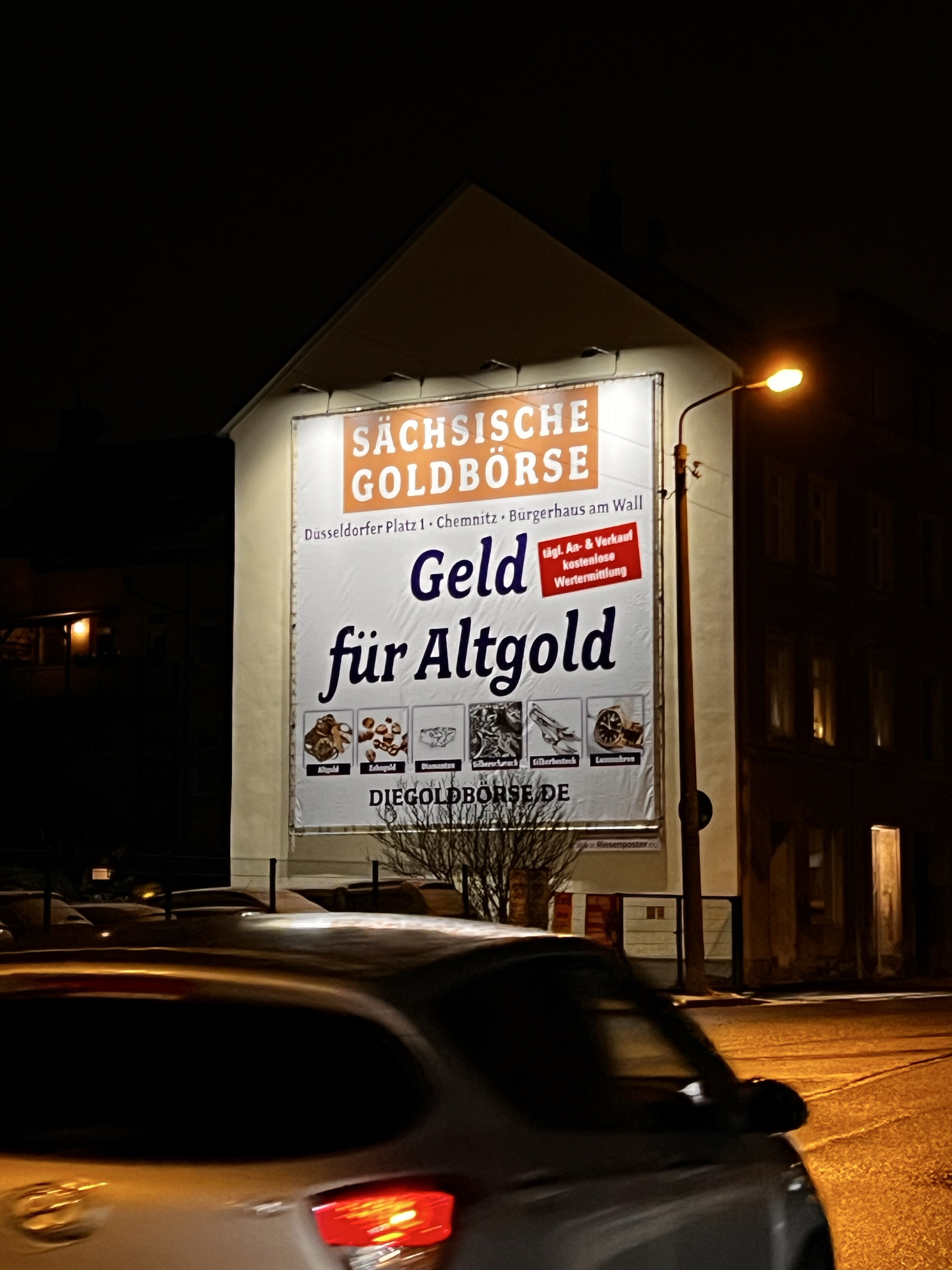 Beleuchtetes Goldbörse-Plakat Geld für Altgold an einer Hausfassade
